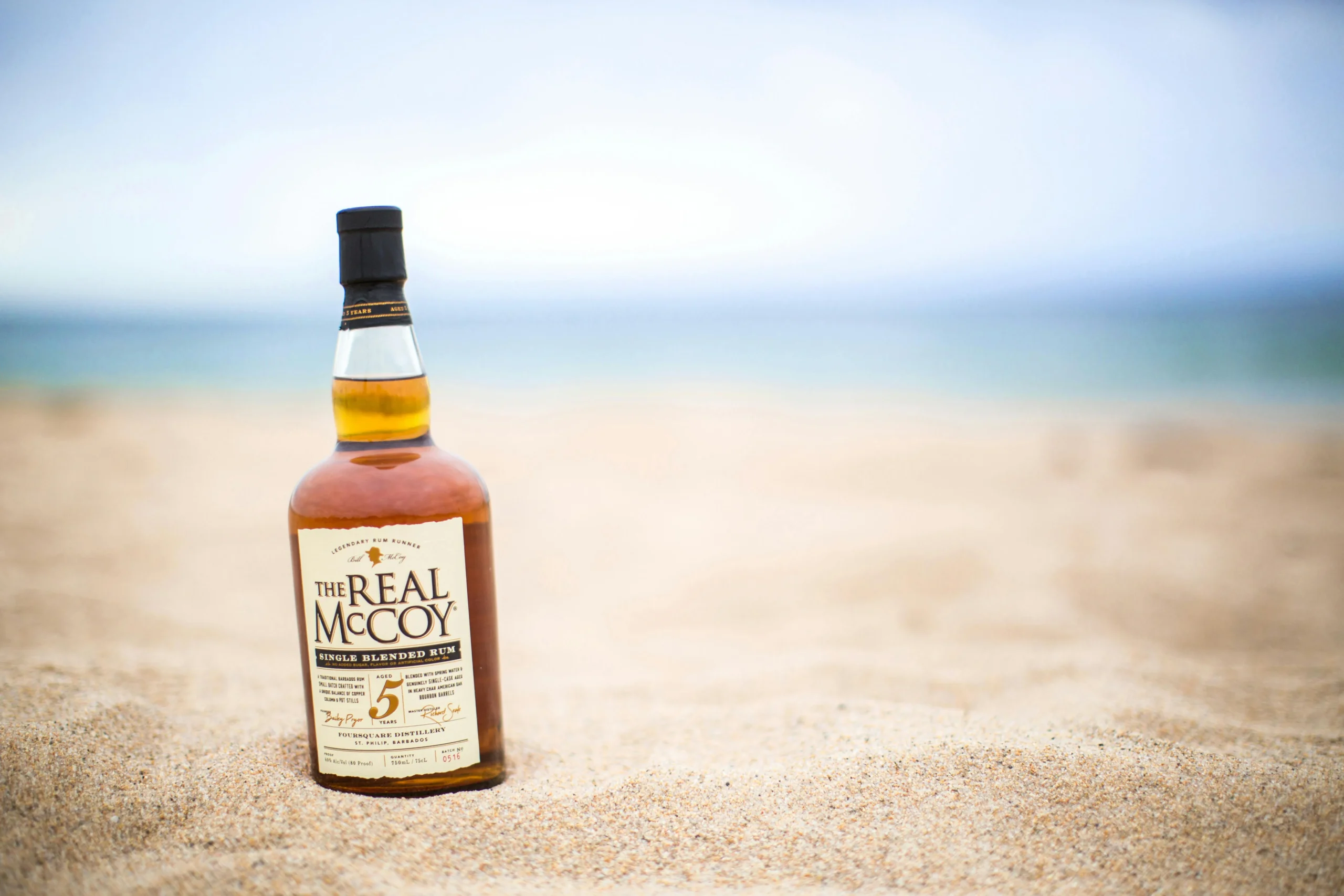 A bottle of The Real McCoy Rum sitting on a picturesque sandy beach, perfect for vacation vibes.