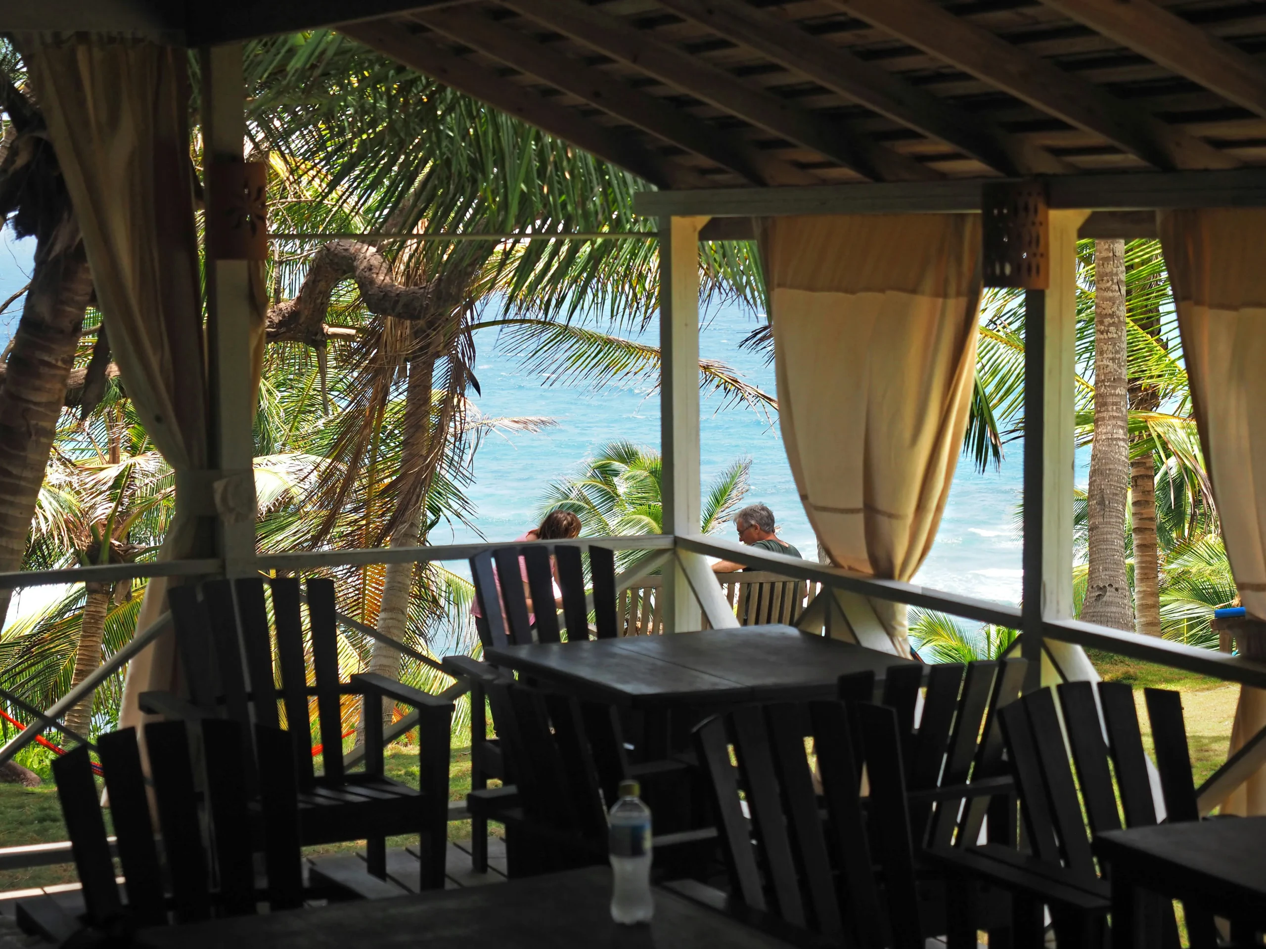 A serene patio view with wooden chairs and palm trees by the ocean in Barbados.