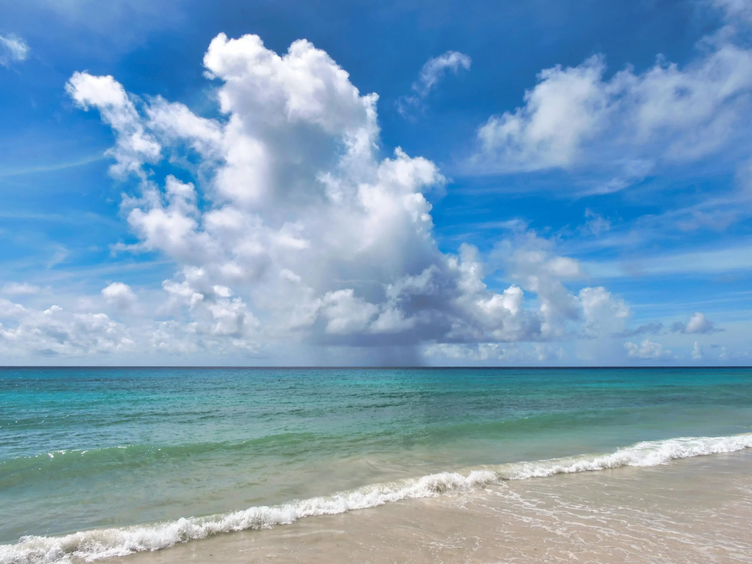 Tranquil ocean scene with dramatic clouds and clear blue water at a Barbados beach.